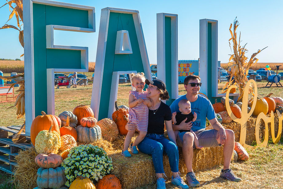 Family posing by large FALL letters at a pumpkin patch