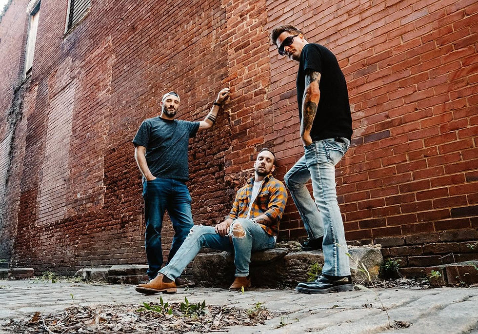 Three men in a band posing against a brick wall alleyway.