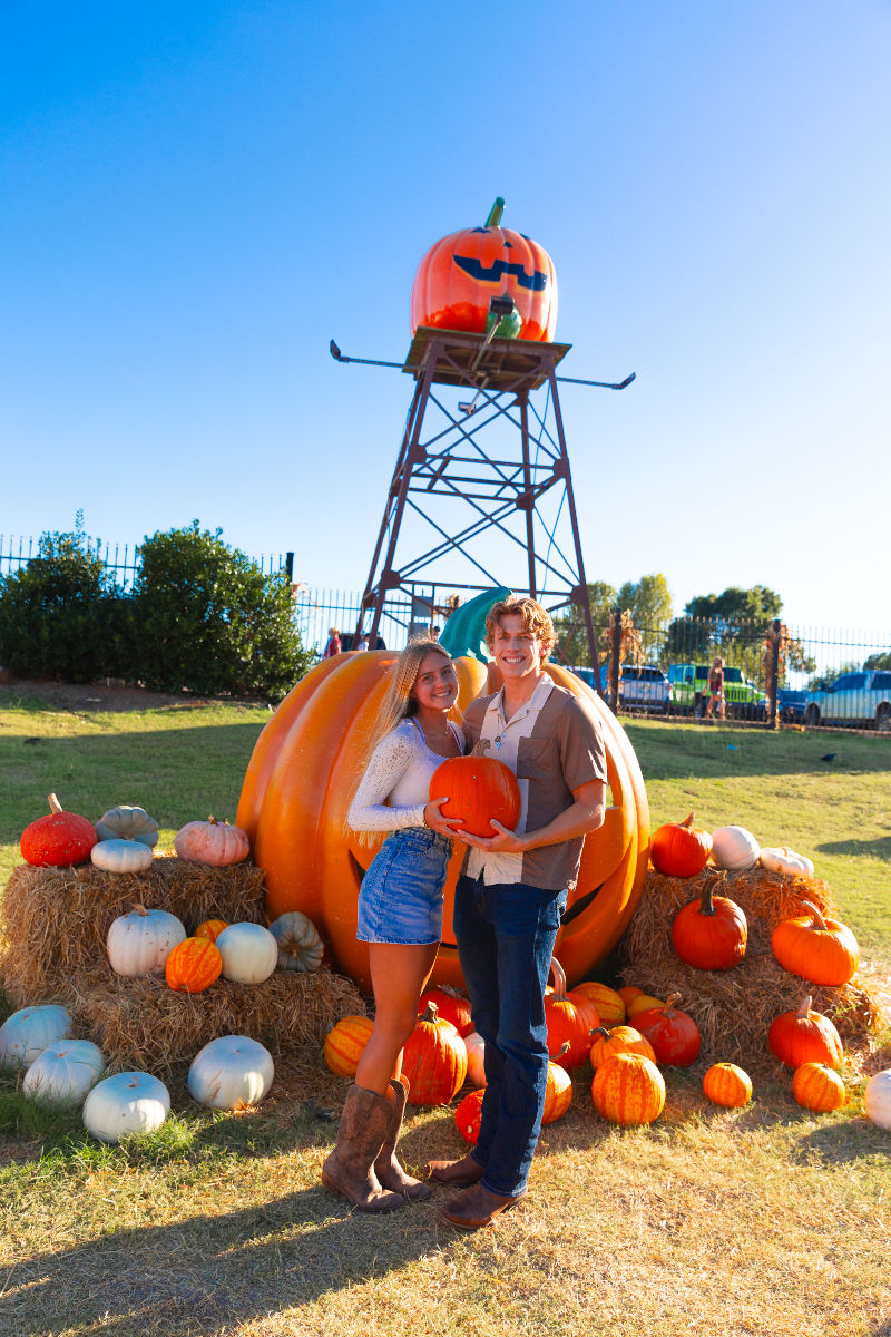 Couple holding a pumpkin at an outdoor patch with displays.