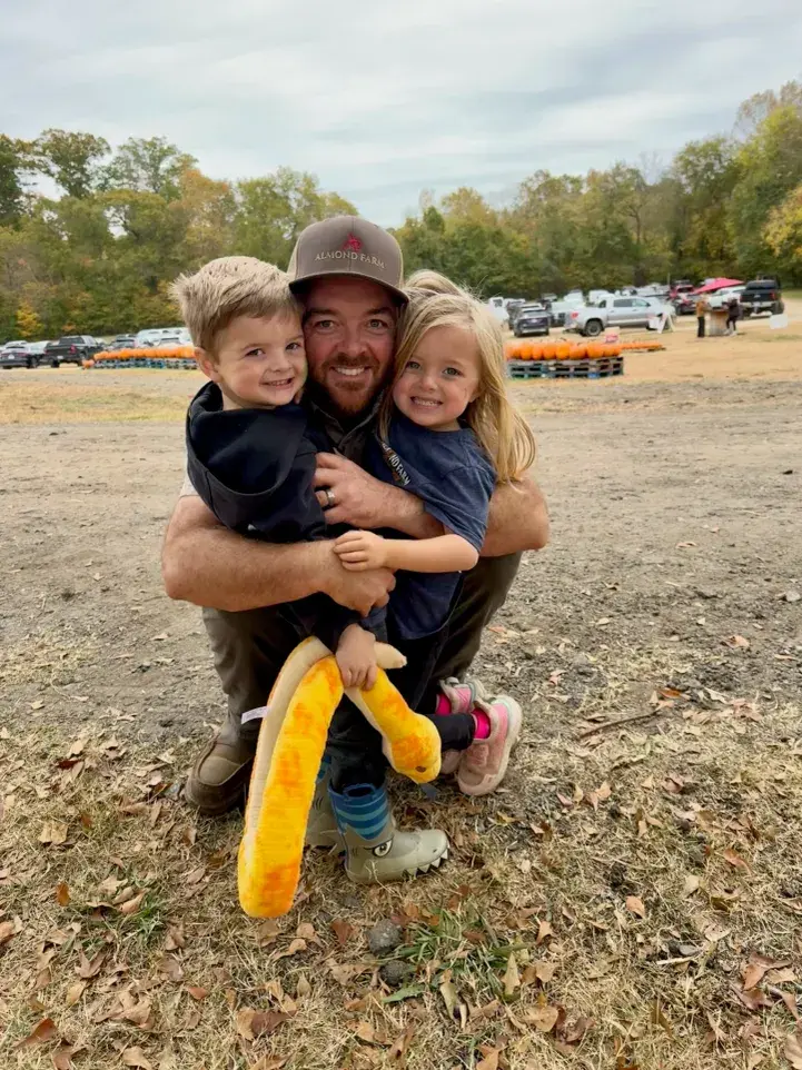 Smiling father hugging two children at a pumpkin patch.
