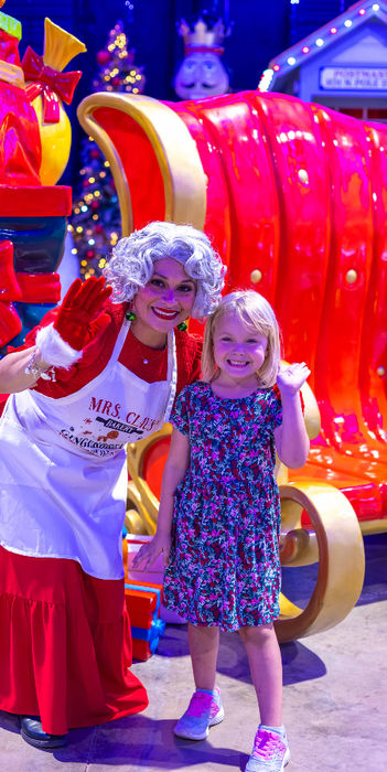 Mrs. Claus and a young girl posing by a Christmas sleigh.