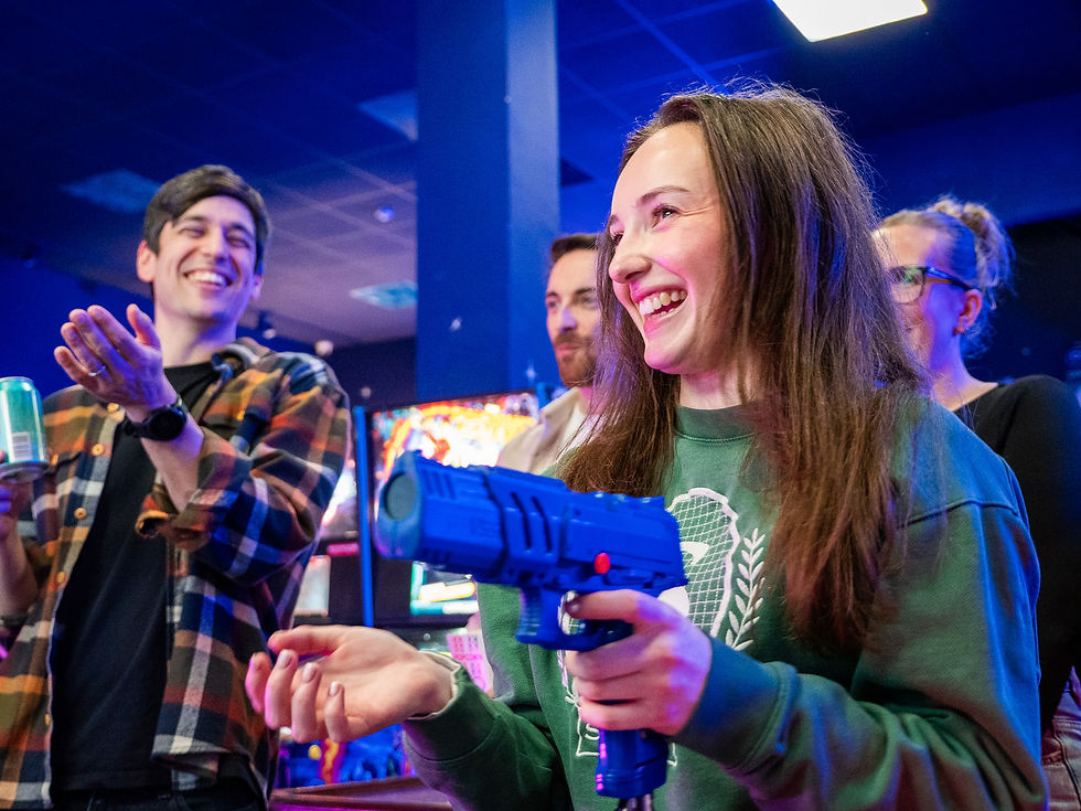 Smiling woman holds blue toy gun, playing game joyfully with friends.