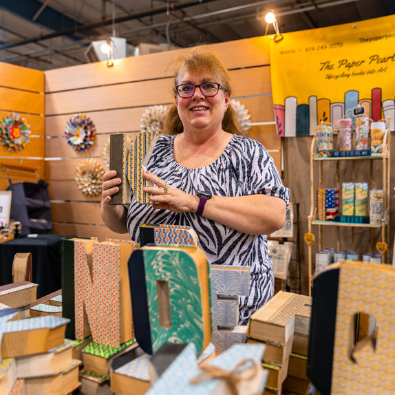 Woman at booth smiling, holding wooden letter art in the shape of a K