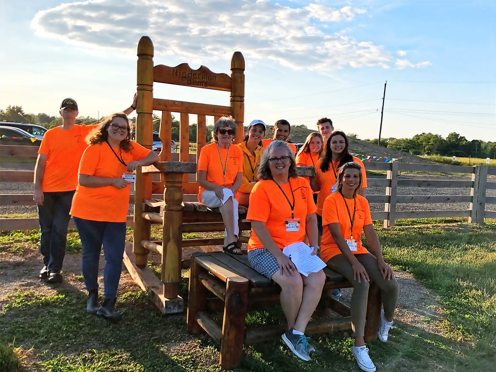 Team of Niederman employees in orange shirts by large wooden chair