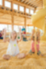 two young girls throw corn in the air in a corn pit