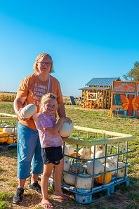 Woman and child holding white pumpkins at a farm outing.