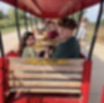 Happy children and adults ride a red miniature outdoor train.