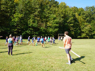 Kids and teens playing an outdoor field game with foam bats during summer youth activities.