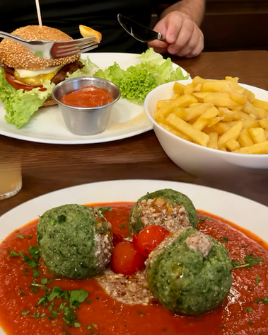 Veganes Abendessen im Restaurant „Zum Wohl“ in Wien: Ein Teller mit Spinatknödeln auf Tomatensauce und ein veganer Burger mit Pommes. Ideal für Blogbeiträge über veganes Essen in Wien, glutenfreie Restaurants und kulinarische Tipps für Städtereisen.