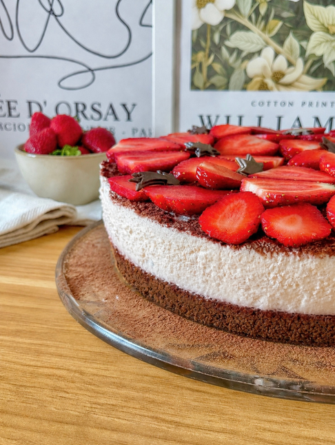 Vegane Schoko-Sahne-Torte mit Erdbeeren auf einer Glasplatte, seitlich fotografiert. Zu sehen sind ein dunkler Schokoladenboden, eine helle Sahnecreme-Schicht, eine feine Kakaoschicht und frische Erdbeerscheiben mit kleiner veganer Schokoladendekoration auf der Oberfläche.