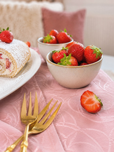 Veganes Erdbeer Dessert mit frischen Erdbeeren, angeschnittener Erdbeerrolle und Puderzucker auf rosa Stoff, einfache Sommer Rezept Idee für vegane Kuchen