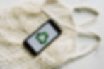 A photo of a white mesh bag laying against a granite background with a cell phone displaying a green recycling symbol on top.