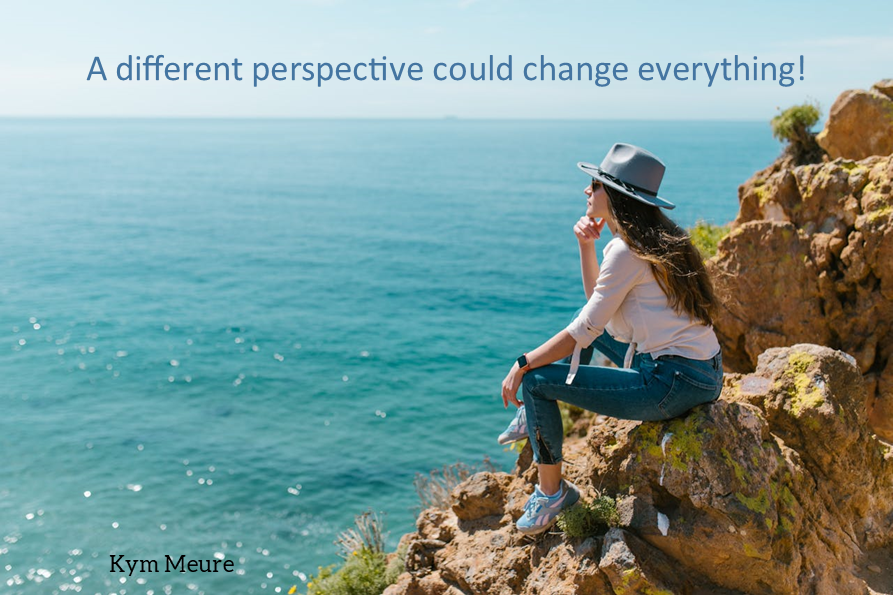Woman in a hat sits on rocky cliff overlooking the sea. Text reads: "A different perspective could change everything!" Mood is contemplative.