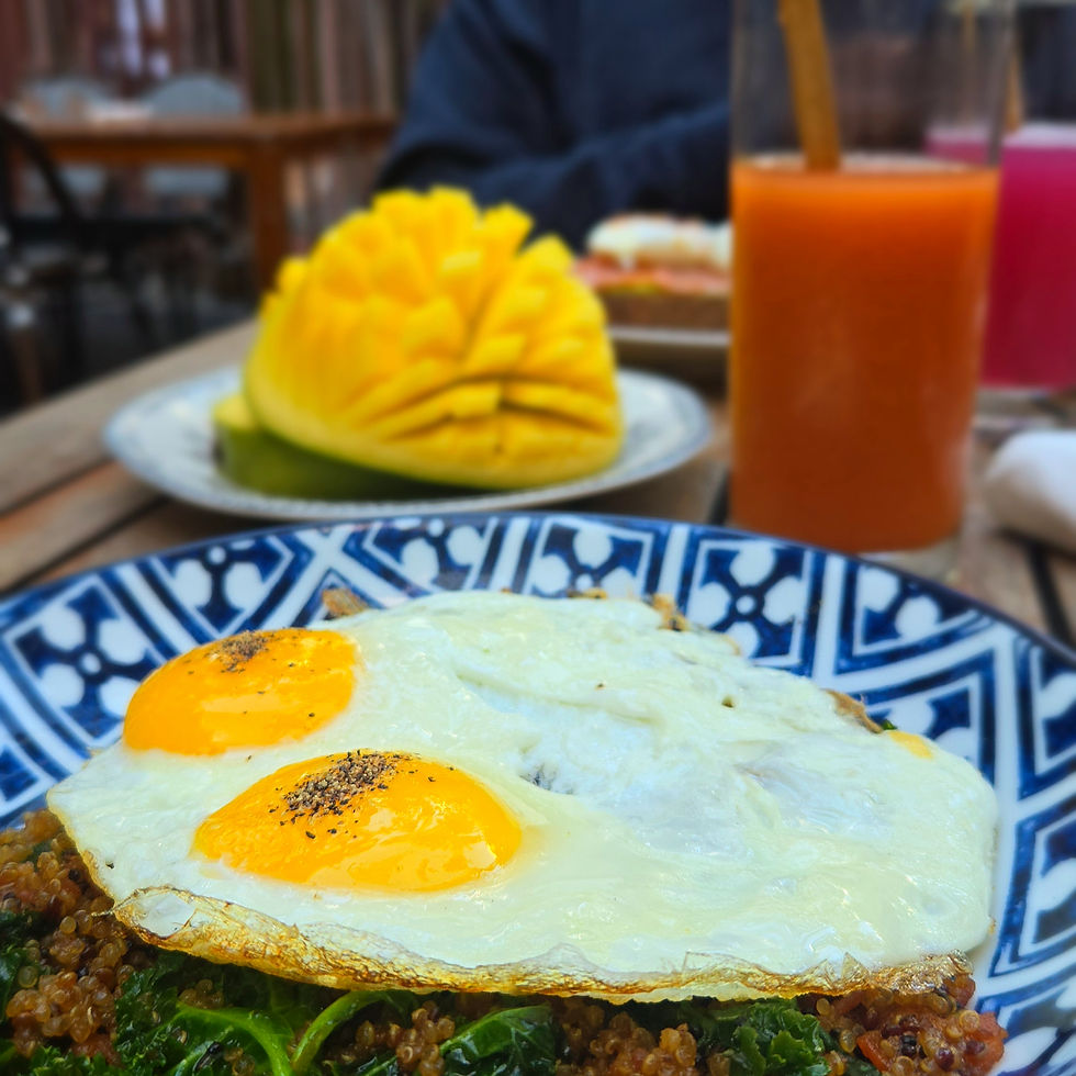A vibrant brunch featuring quinoa topped with sunny side up eggs, served with a fresh mango and a glass of carrot juice.