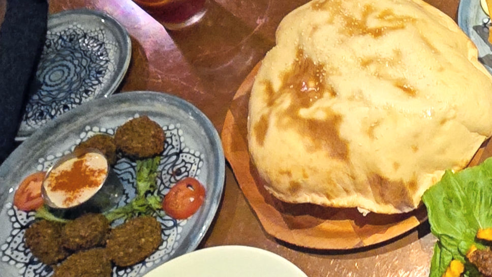A freshly baked lava bread sits puffed up and golden brown on a wooden serving board, accompanied by a plate of falafel and garnishes, ready to be savored.