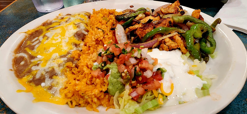 A vibrant Mexican dish featuring cheesy refried beans, flavorful rice, grilled chicken with bell peppers and onions, accompanied by fresh pico de gallo, guacamole, and a spoonful of sour cream.