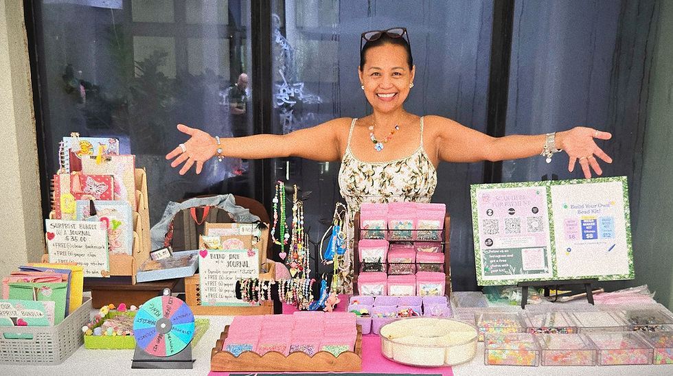 A joyful me enthusiastically showcases my colorful display of handmade, journals, and crafting kits at a vibrant market stall.