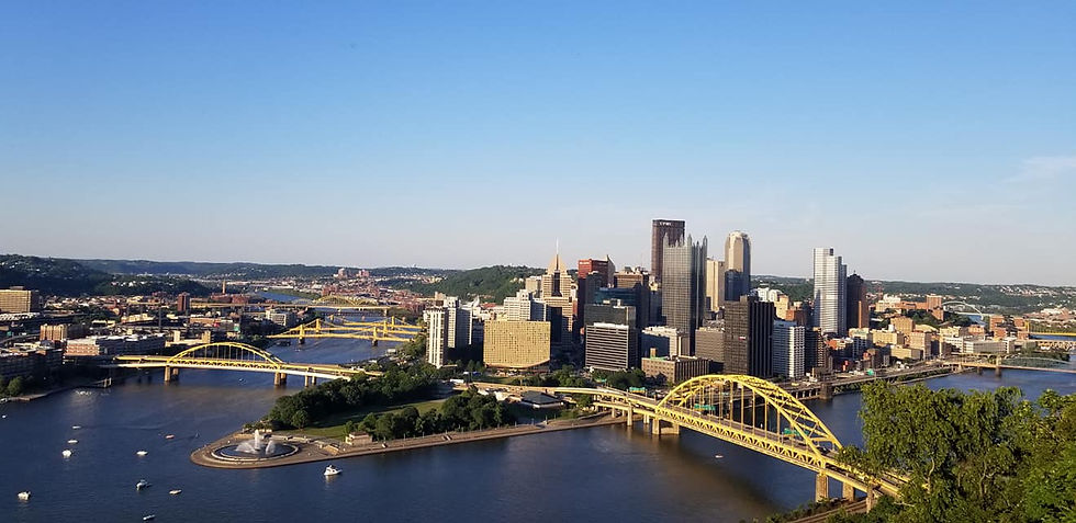 A breathtaking view of Pittsburgh's skyline, featuring its iconic yellow bridges stretching across the rivers beneath a clear blue sky.