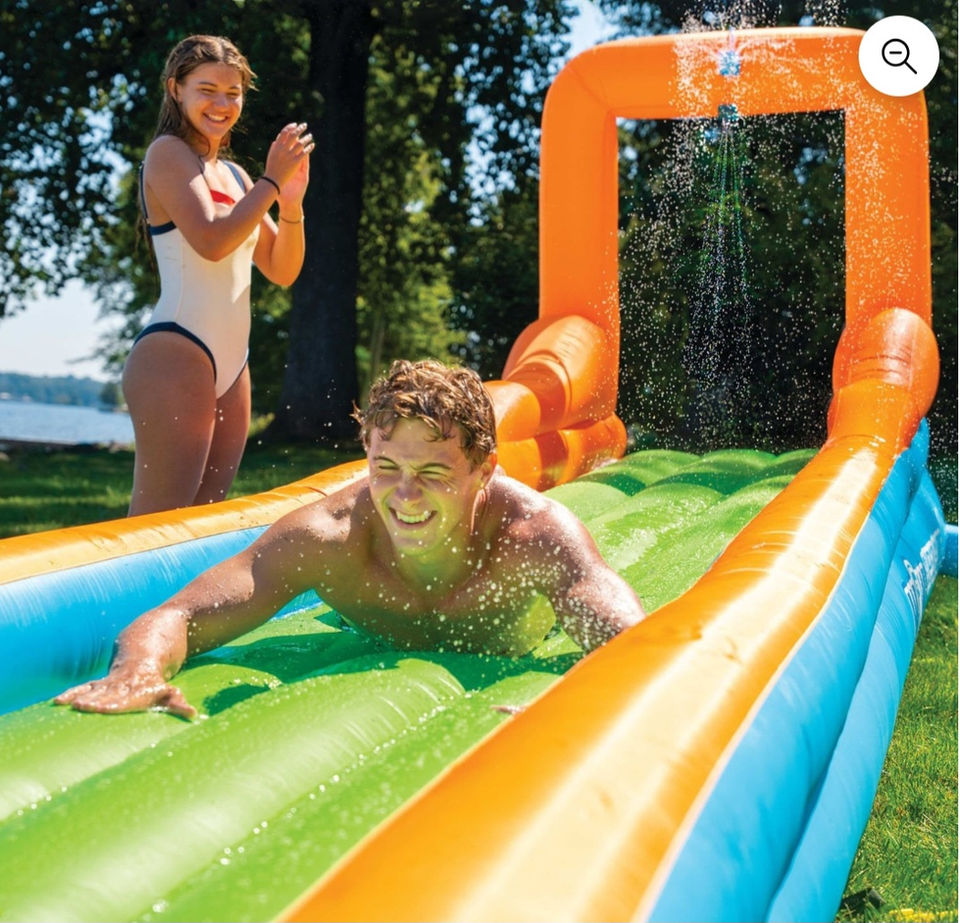 Young man sliding on a colorful backyard water slide.