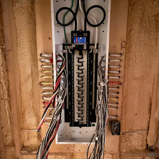 An electrical panel upgrade in progress – Phase 1. The image shows an open electrical panel with disconnected wires and new breakers being installed.