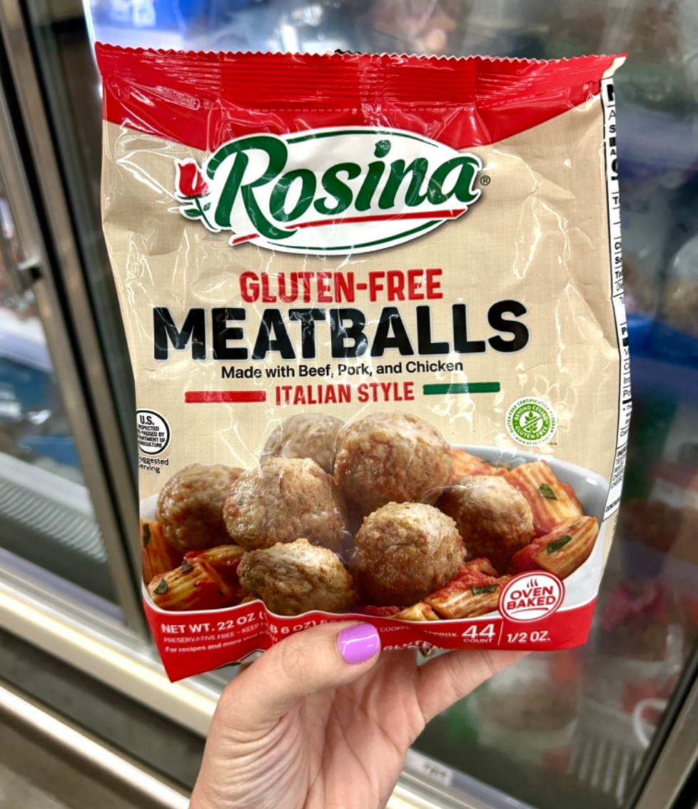 A hand holds a package of Rosina Gluten-Free Italian Style Meatballs in an HEB grocery store freezer aisle.