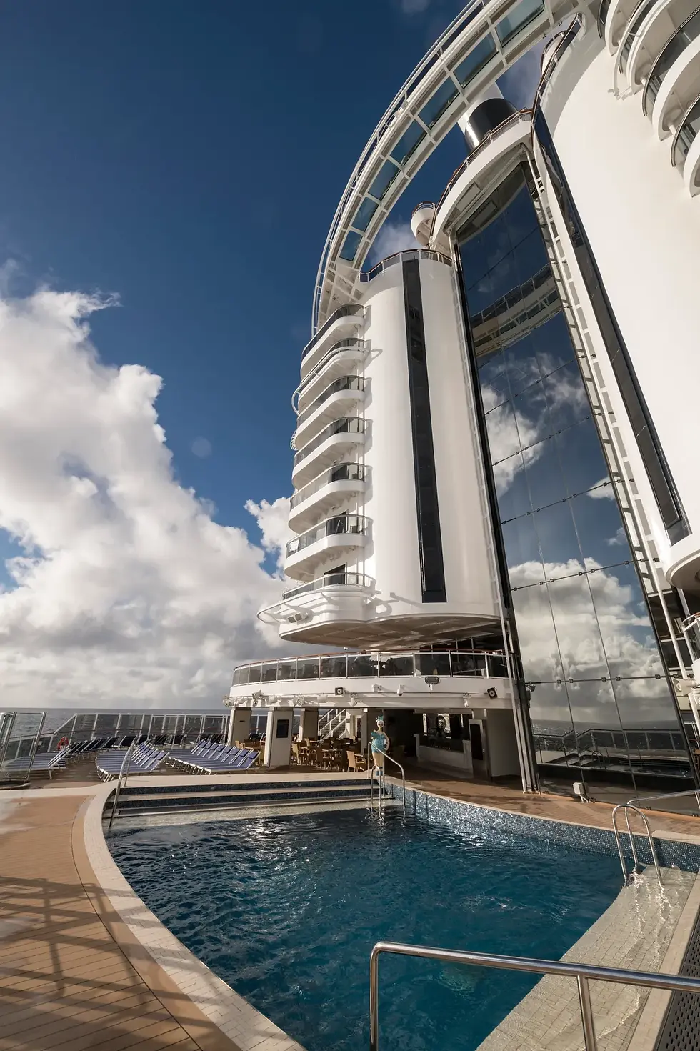 Aboard the MSC Seaside-class ship, an impressive blend of terraced balconies and sleek glass panels complement a modern pool deck under a vibrant sky.
