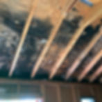 Wooden ceiling beams with dark water damage. The room has unfinished walls and exposed wood, creating a rustic and neglected atmosphere.