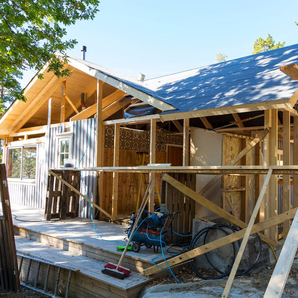 Wooden house under construction with visible beams and plywood. Blue sky backdrop. Tools and cables scattered on the wooden deck.