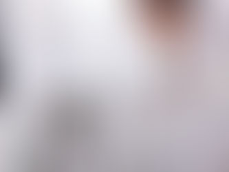 Woman examining mold on a white wall near a window with blinds. She looks concerned, wearing a white top. Bright indoor setting.