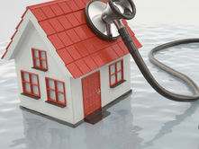 A stethoscope on a small red-roofed house standing in water, suggesting a home health check. Calm atmosphere with reflections visible.