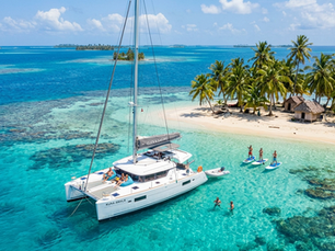 Catamarán de lujo anclado en aguas turquesas de Guna Yala con huéspedes haciendo paddle board cerca de una isla vírgen de palmeras.