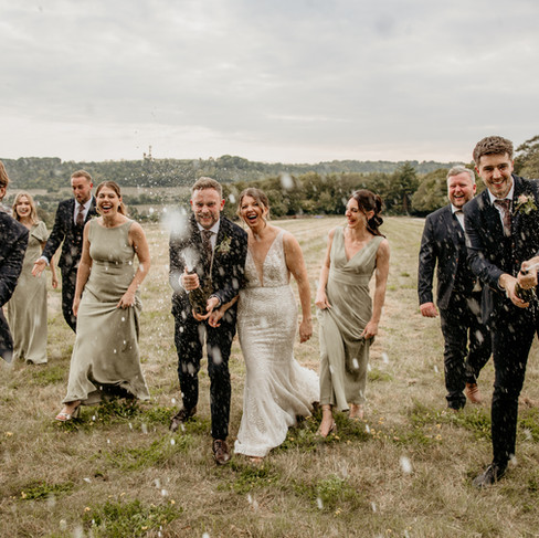 The Bridal Party shaking champagne bottles in a field.