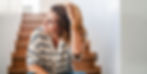Woman in perimenopause sitting on staircase running hand through hair.