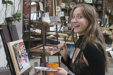 An artist is painting on a canvas, set on an easel, in the gallery.