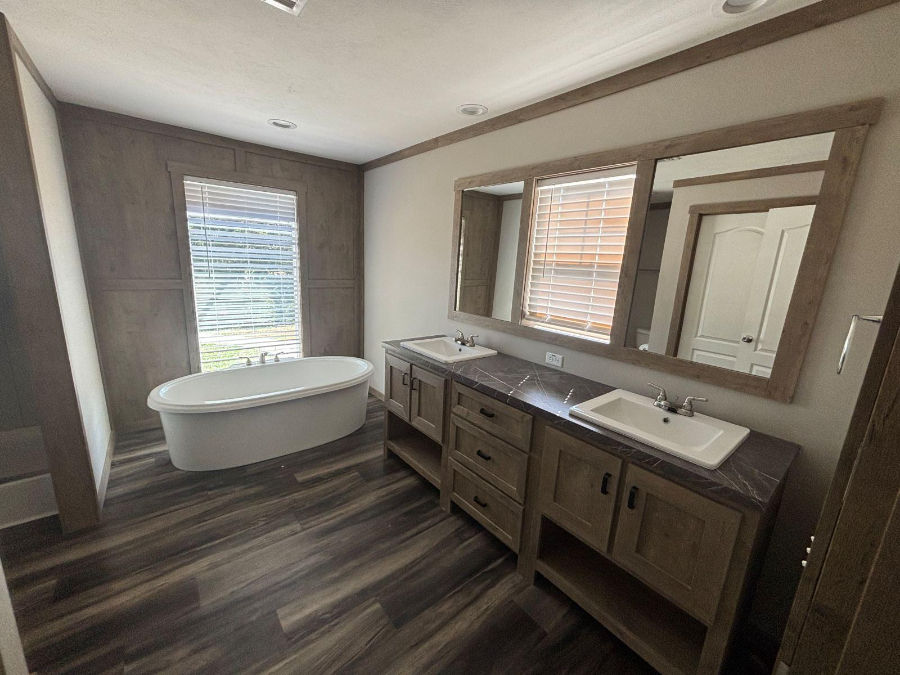 Modern bathroom with a freestanding tub, double sink vanity, large mirror, wooden floor, and a window with blinds. Calm and inviting mood.