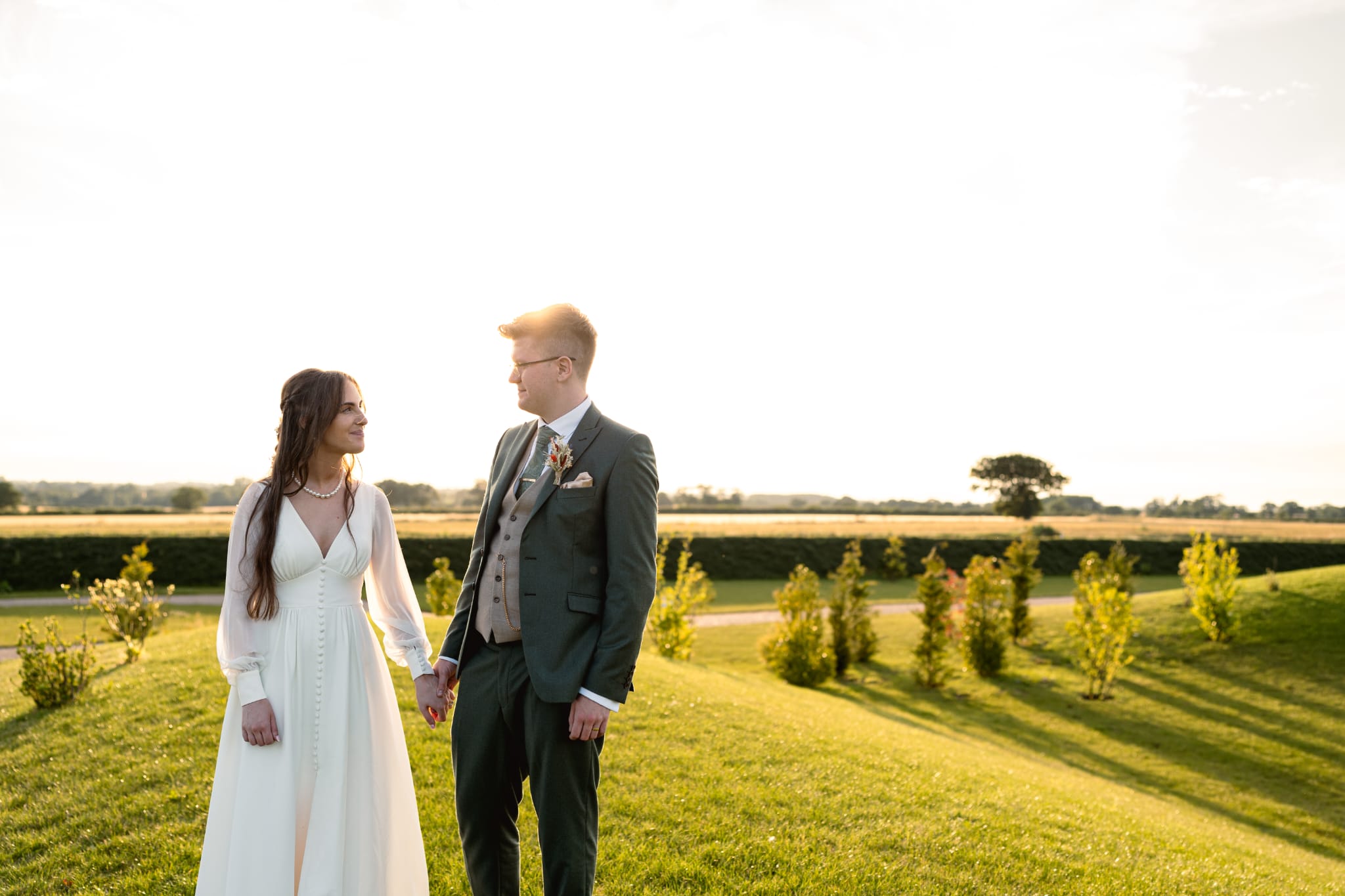bride and groom looking at each other and holding hands in field