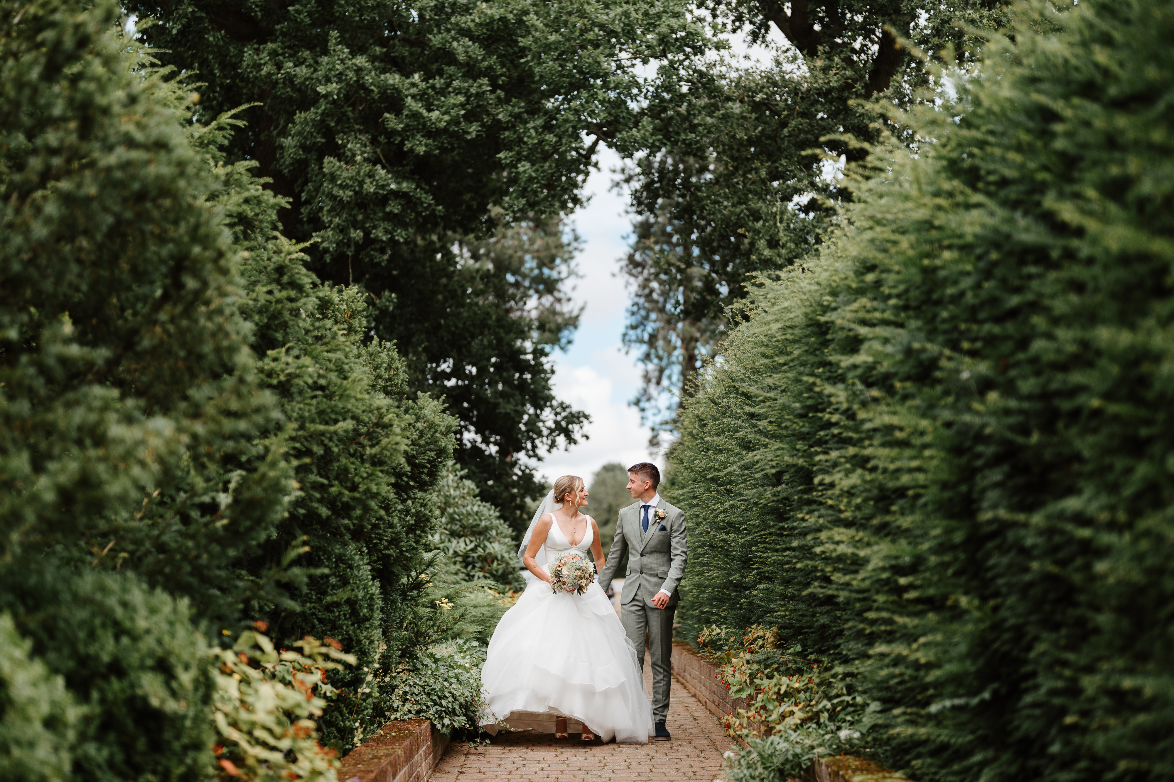 bride and groom looking at each other walking down path outside surrounded by bushes
