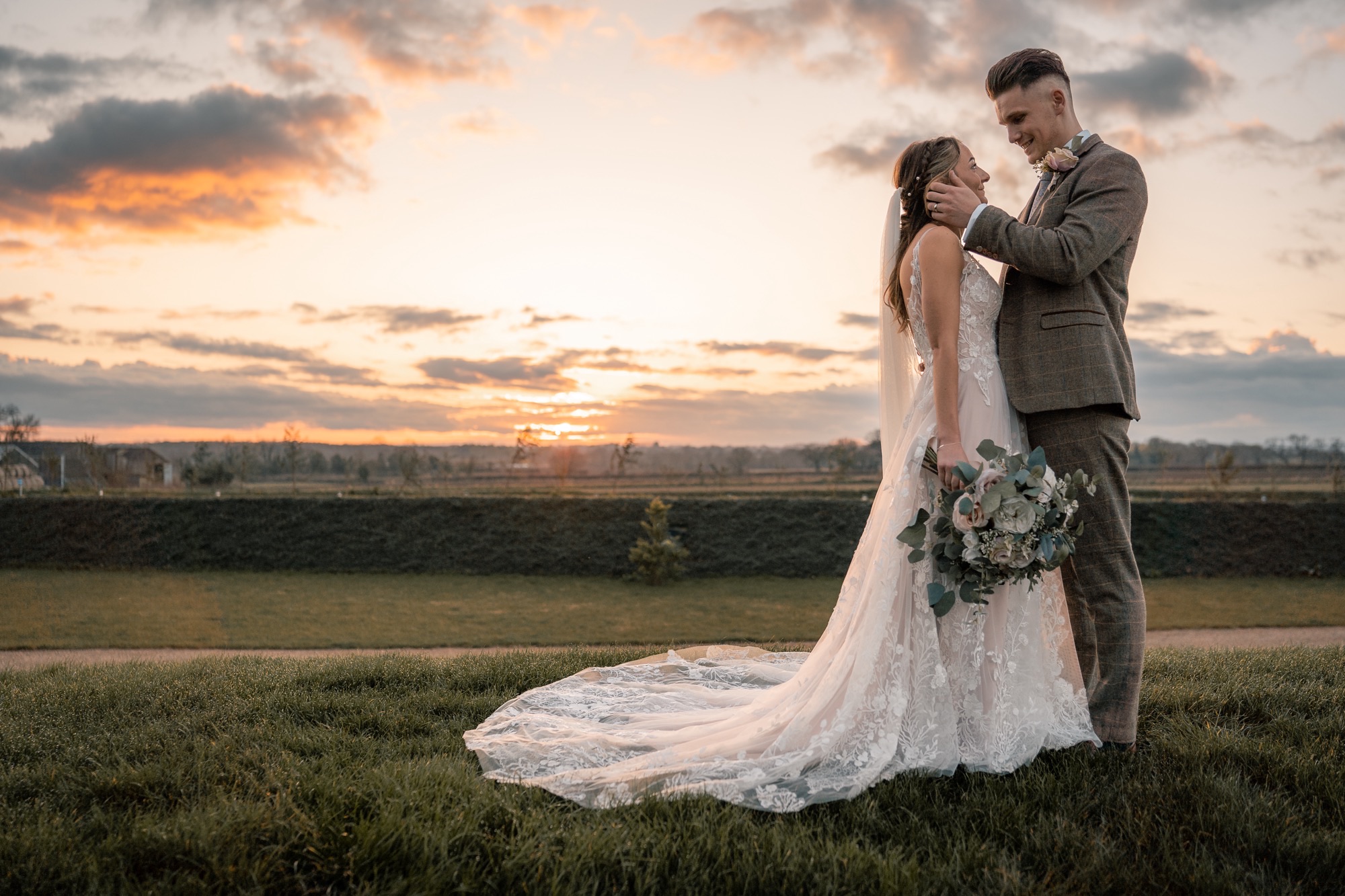 groom holding bride's face in a field with a sunset in the background