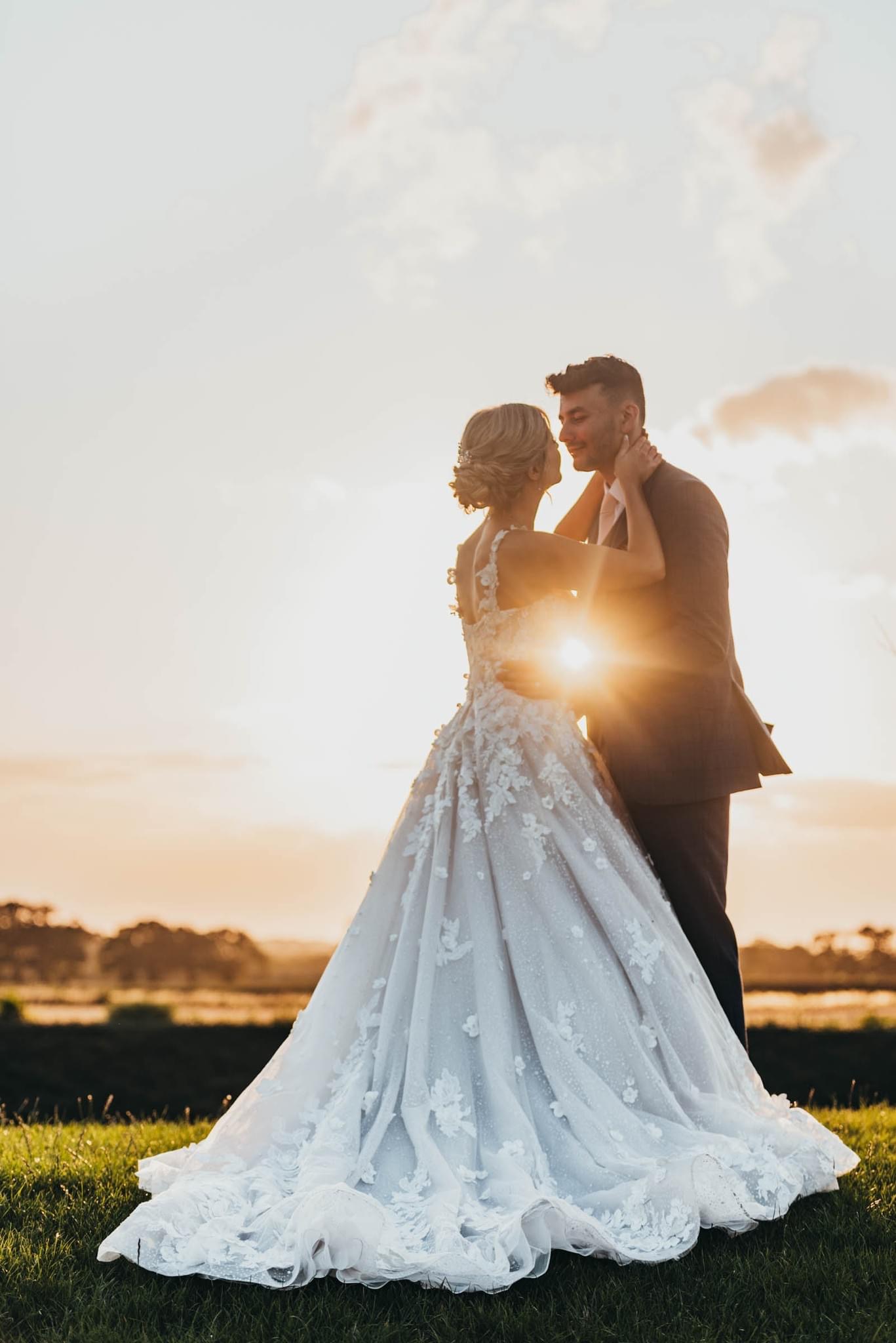 bride and groom looking at each other in field with evening sun in the background