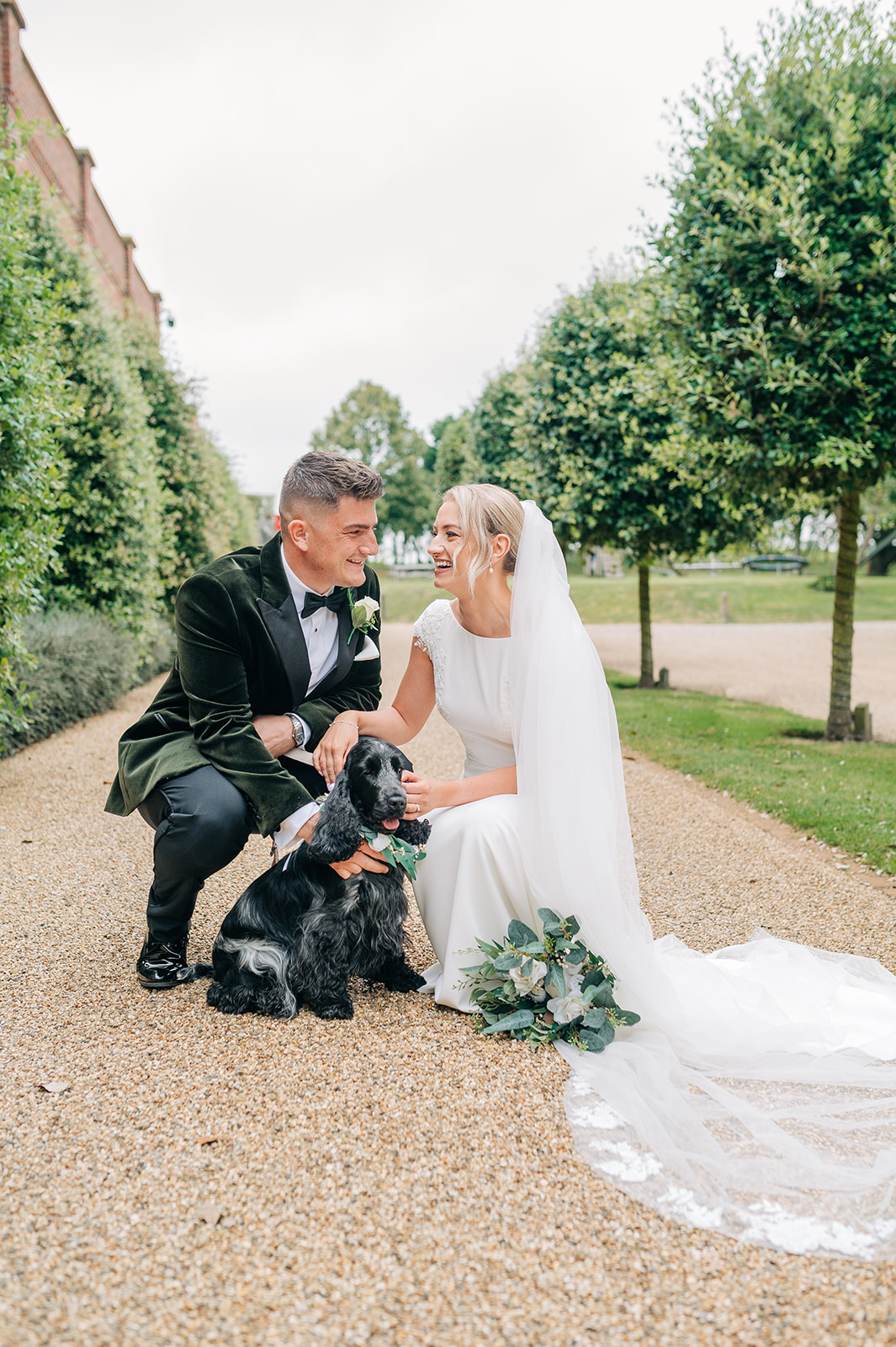 bride and groom knelt down with dog outside with trees in background