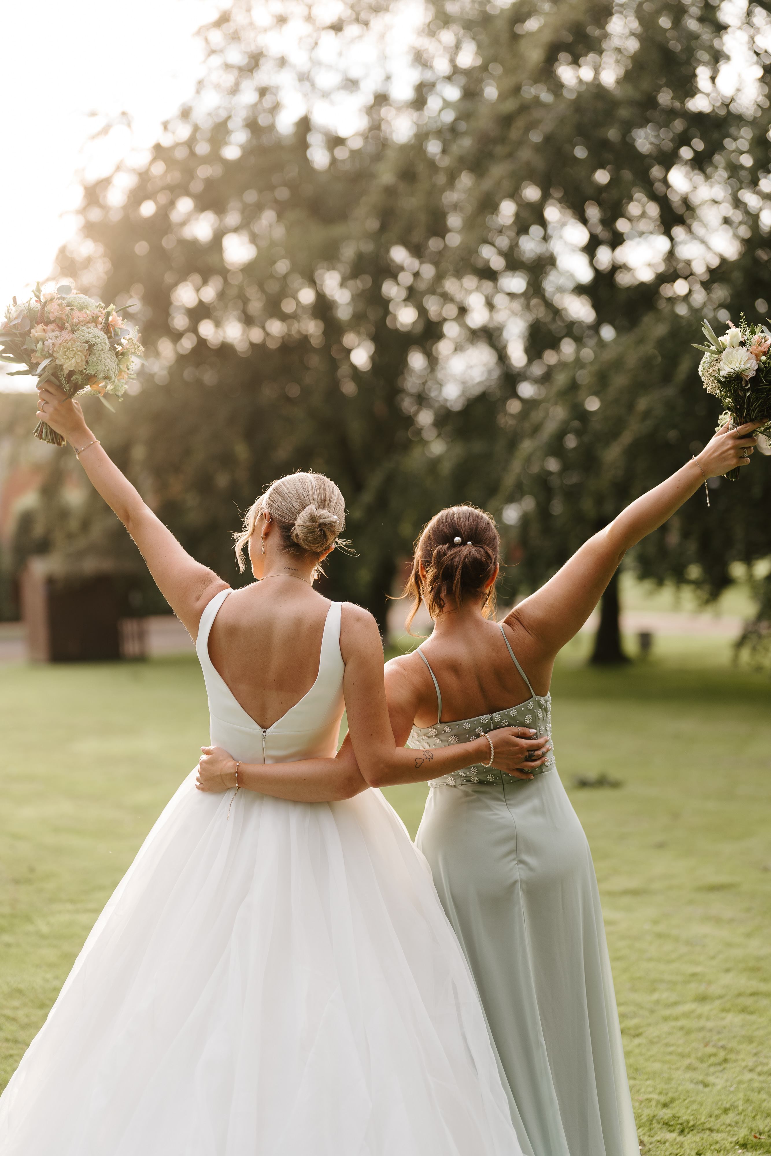 bride and bridesmaid stood outside with arms around each other photographed from behind