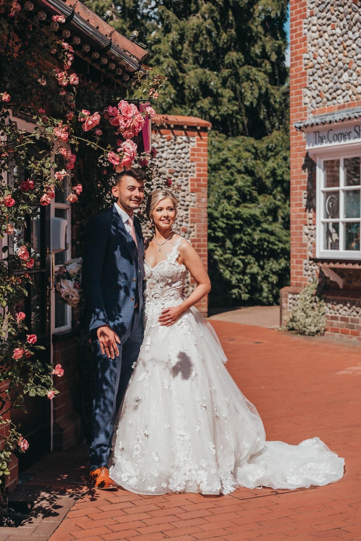 bride and groom stood outside brick building covered in flowers
