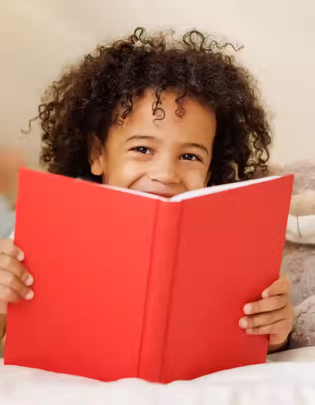 A young and happy child enjoys reading a bright red book.