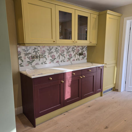 Kitchen area with solid oak flooring installed with kitchen wall units yellow in colour and base units red in colour.