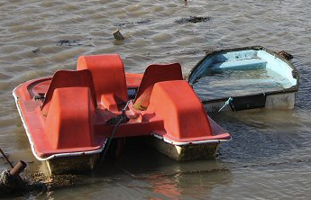 A pedalo, a scruffy red seaside pedal boat and a blue rowing boat filled with water tied together