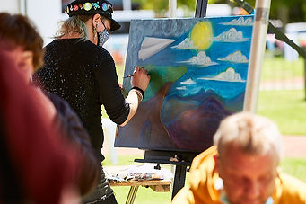 FestvalOfNow Credit Fokus Creative. Kat in front of a canvas, being interviewed on camera at a festival in park