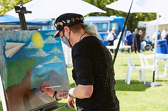 Kat Coppock FestvalOfNow Credit Fokus Creatives. FestvalOfNow Credit Fokus Creative. Kat paints a canvas at a festival in a park