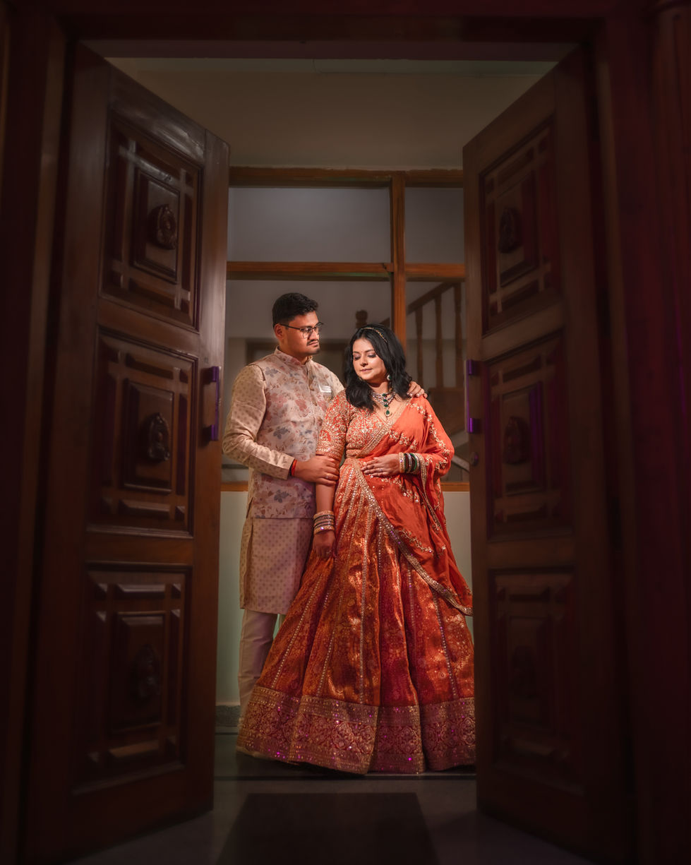Couple in traditional attire standing by wooden doors.
