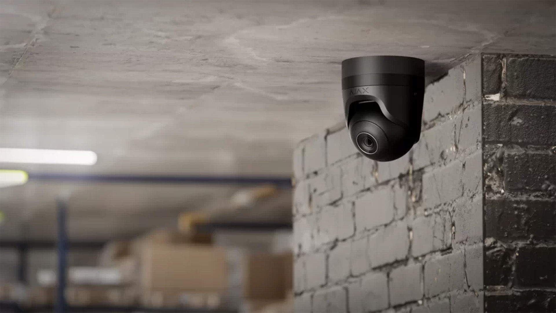 Security camera, black, mounted on ceiling, brick wall, monitoring warehouse.