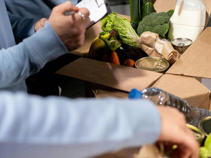 Close-up of volunteers organising food donations, showing an open box filled with canned and fresh food, and milk